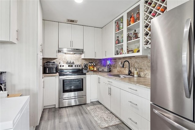 kitchen with stainless steel appliances, decorative backsplash, white cabinets, sink, and light hardwood / wood-style floors