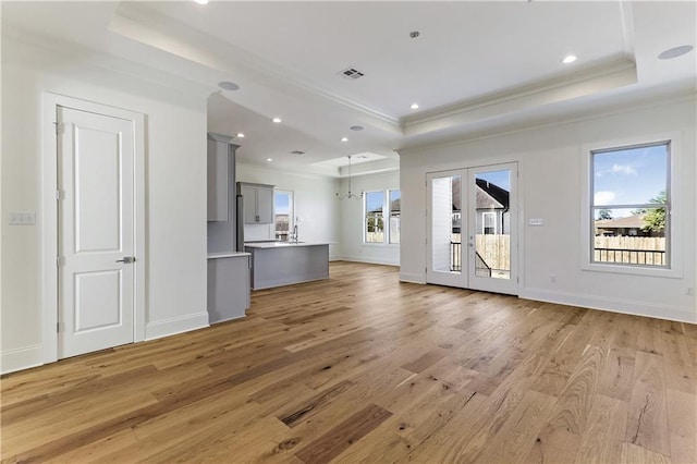 unfurnished living room featuring a raised ceiling, a healthy amount of sunlight, light hardwood / wood-style flooring, and french doors