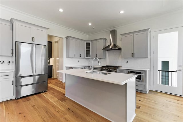 kitchen with wall chimney range hood, light wood-type flooring, stainless steel appliances, and sink