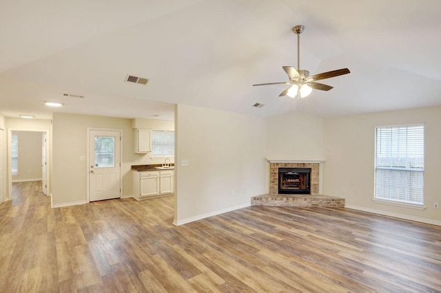 unfurnished living room featuring light hardwood / wood-style flooring, lofted ceiling, ceiling fan, a fireplace, and sink