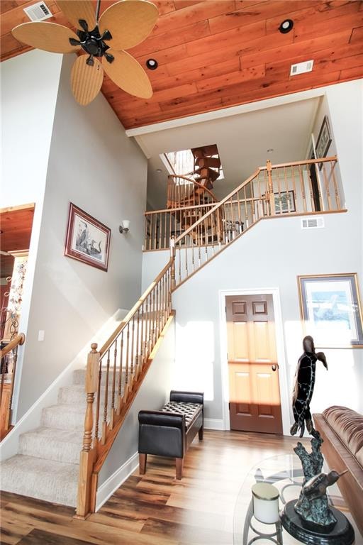 staircase featuring ceiling fan, wooden ceiling, hardwood / wood-style floors, and a towering ceiling