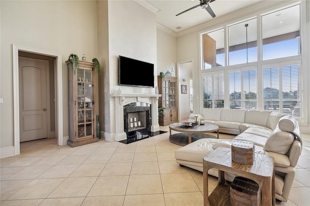 tiled living room featuring a high end fireplace, ceiling fan, a high ceiling, and crown molding