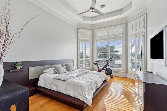 bedroom featuring a tray ceiling, ornamental molding, ceiling fan, and light hardwood / wood-style floors