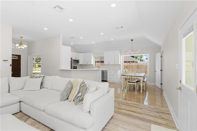 living room with light hardwood / wood-style flooring, plenty of natural light, a notable chandelier, and vaulted ceiling