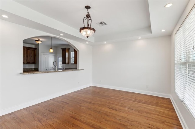 unfurnished living room with sink, a tray ceiling, and hardwood / wood-style floors