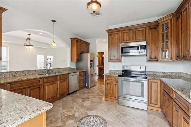 kitchen featuring light stone counters, sink, decorative light fixtures, and stainless steel appliances