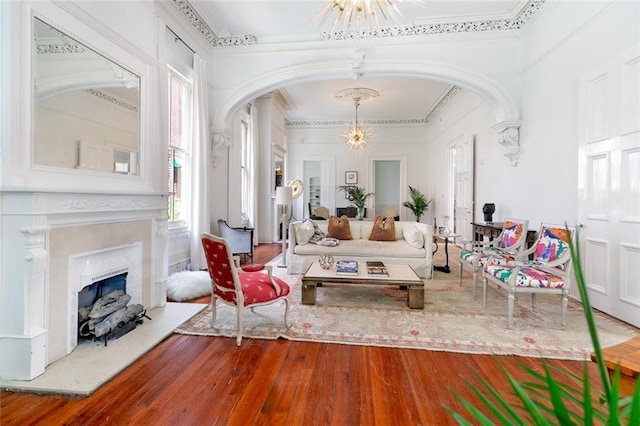 living area with a fireplace with raised hearth, ornamental molding, hardwood / wood-style floors, arched walkways, and a chandelier