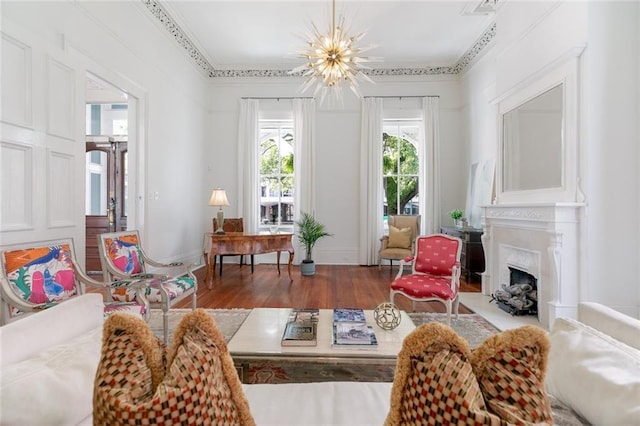 living area featuring wood finished floors, baseboards, a fireplace with flush hearth, ornamental molding, and a chandelier