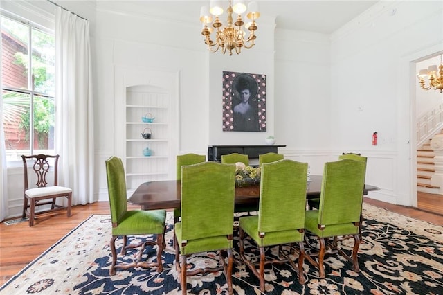 dining room featuring built in shelves, wood finished floors, an inviting chandelier, ornamental molding, and stairs