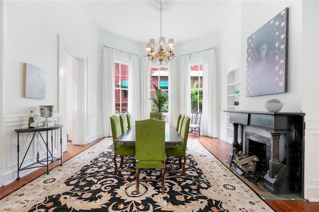 dining area featuring wood finished floors, a premium fireplace, crown molding, a decorative wall, and a chandelier