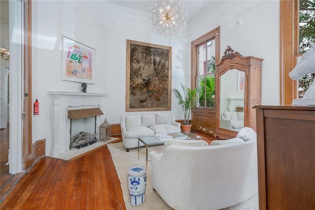 living area with a notable chandelier, a fireplace with flush hearth, crown molding, and wood finished floors