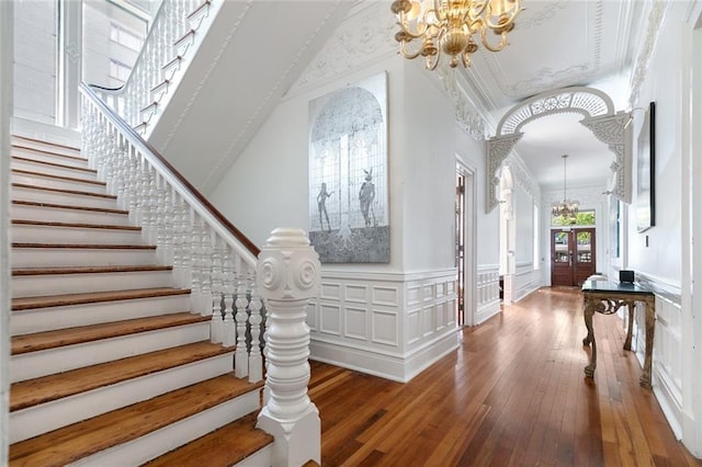 foyer entrance featuring a wainscoted wall, stairs, an inviting chandelier, hardwood / wood-style flooring, and a decorative wall