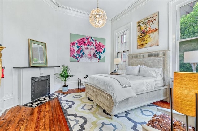 bedroom featuring baseboards, a chandelier, a fireplace with flush hearth, ornamental molding, and wood finished floors