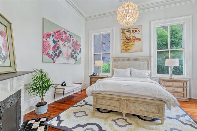 bedroom featuring a notable chandelier, a fireplace, wood finished floors, and crown molding