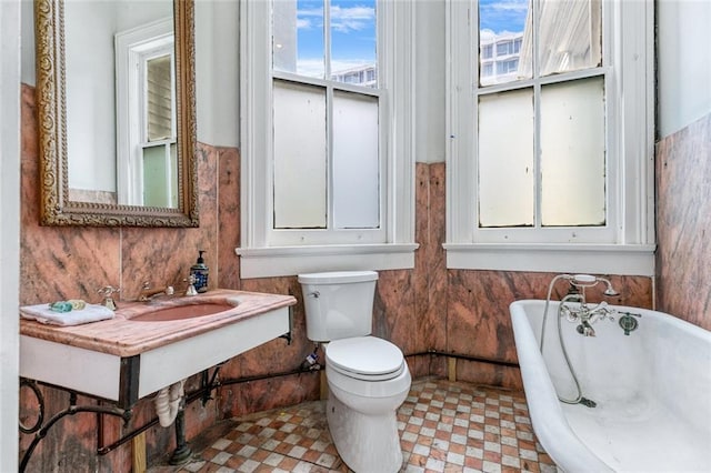 bathroom featuring a soaking tub, toilet, tile patterned floors, and wood walls