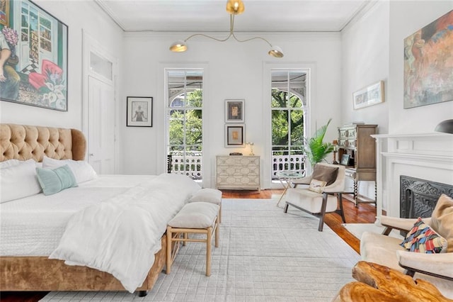 bedroom featuring access to exterior, wood finished floors, a fireplace, and ornamental molding