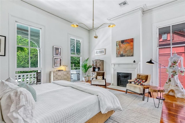 bedroom featuring visible vents, a fireplace with raised hearth, ornamental molding, and wood finished floors