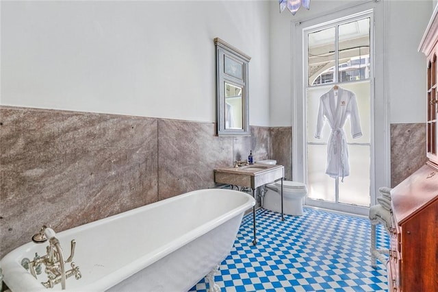 bathroom with a wainscoted wall, toilet, tile walls, and a freestanding tub