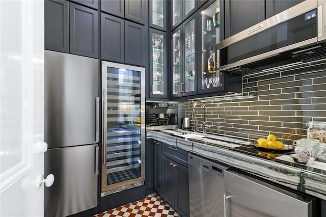 kitchen featuring beverage cooler, light stone countertops, stainless steel appliances, decorative backsplash, and glass insert cabinets