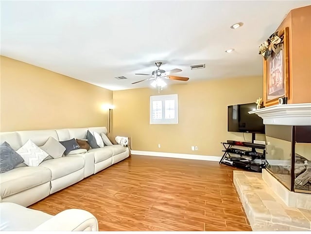 living room with a fireplace, wood-type flooring, and ceiling fan