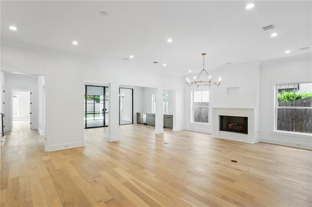 unfurnished living room with an inviting chandelier, a wealth of natural light, and light hardwood / wood-style floors