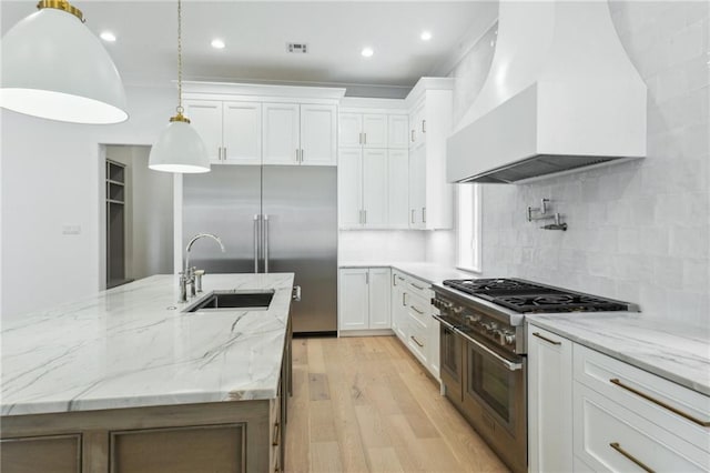 kitchen featuring decorative light fixtures, white cabinetry, custom exhaust hood, range with two ovens, and light stone counters