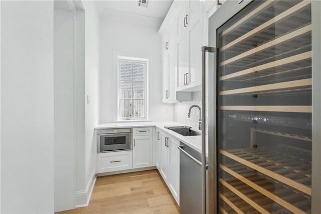 kitchen with wine cooler, sink, stainless steel dishwasher, light hardwood / wood-style floors, and white cabinets