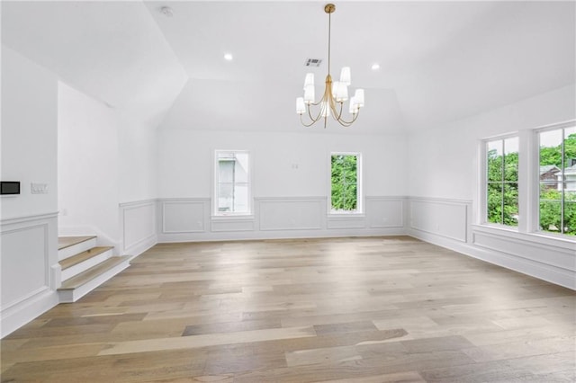 unfurnished dining area featuring an inviting chandelier, vaulted ceiling, and light hardwood / wood-style floors