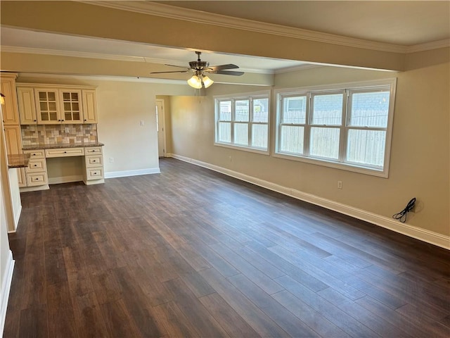 unfurnished living room with ceiling fan, dark hardwood / wood-style flooring, ornamental molding, and built in desk