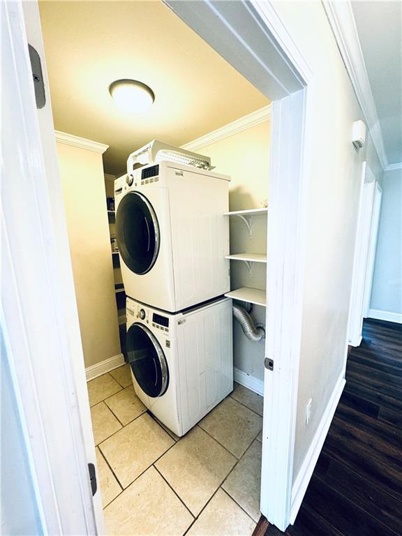 laundry area featuring crown molding, stacked washer / drying machine, and light tile patterned floors