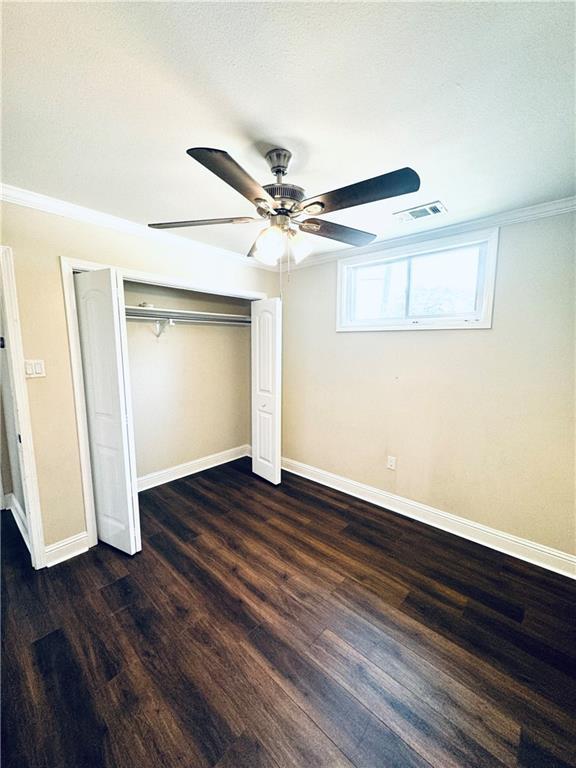 unfurnished bedroom featuring crown molding, dark wood-type flooring, ceiling fan, and a closet