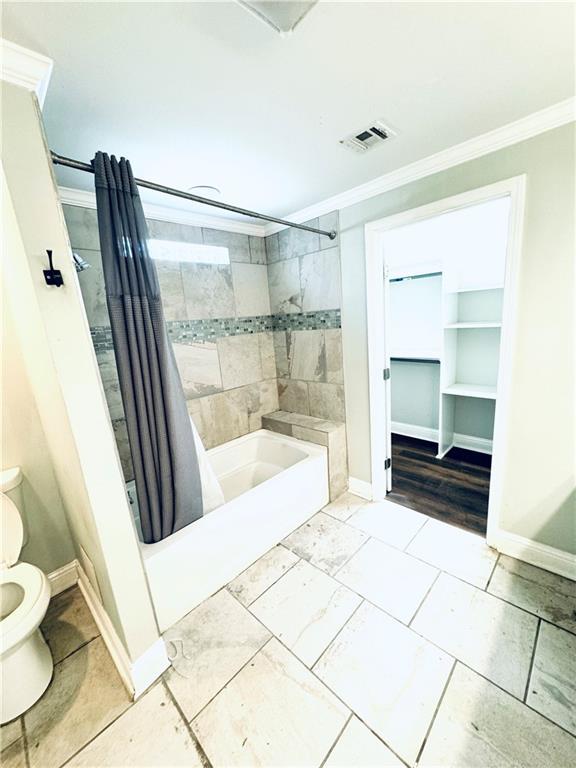 bathroom featuring tile patterned floors, shower / bathtub combination with curtain, toilet, and ornamental molding