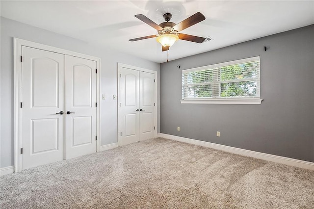 unfurnished bedroom with carpet, two closets, and ceiling fan