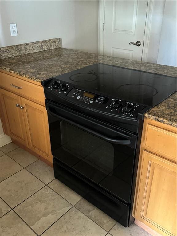 kitchen with dark stone countertops, electric range, and light tile patterned flooring