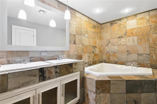 bathroom with tile walls, dual bowl vanity, and tiled bath