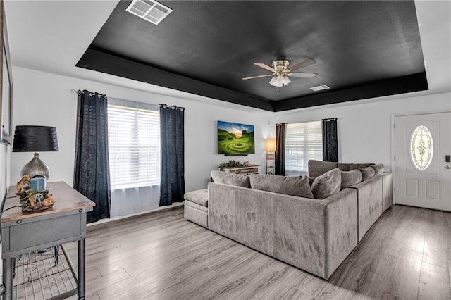 living room with ceiling fan, a tray ceiling, and wood-type flooring