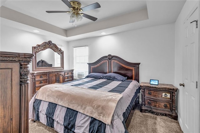 carpeted bedroom featuring ceiling fan and a raised ceiling