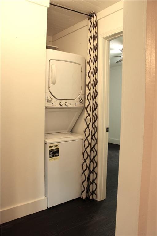 washroom with baseboards, stacked washer and dryer, dark wood-style flooring, and laundry area