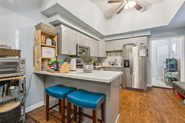 kitchen with stainless steel appliances, dark wood finished floors, a sink, a peninsula, and light countertops