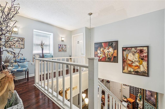 corridor with baseboards, an upstairs landing, a textured ceiling, and wood finished floors