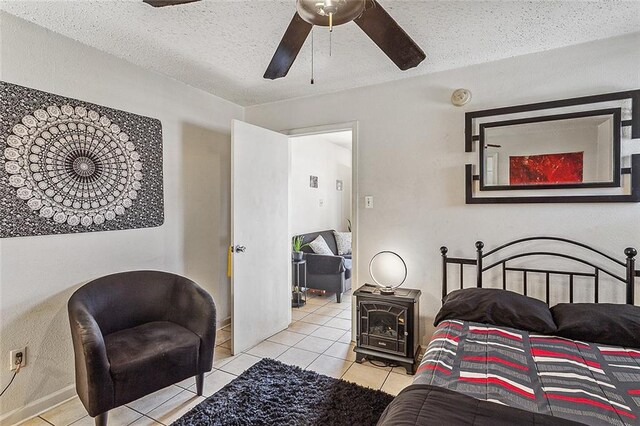 tiled bedroom with ceiling fan, a textured ceiling, and a wood stove