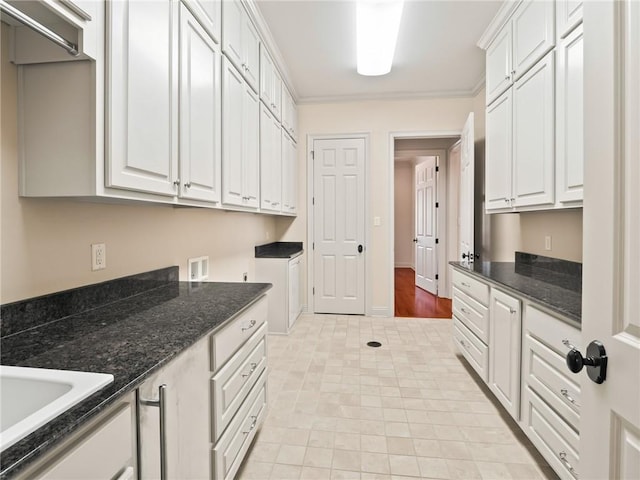 kitchen featuring dark stone countertops, light tile patterned floors, crown molding, and white cabinetry