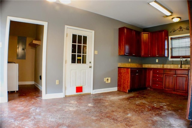 kitchen featuring concrete flooring, electric panel, washer / dryer, and sink