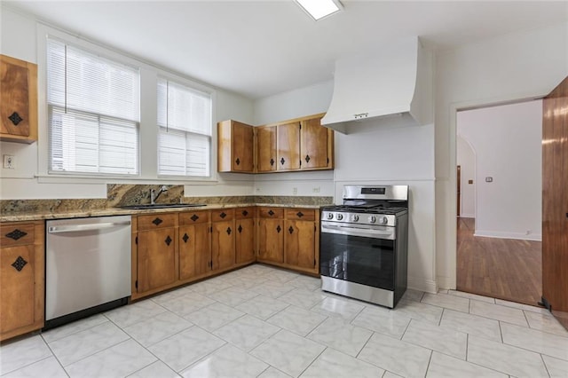 kitchen featuring sink, appliances with stainless steel finishes, range hood, light stone countertops, and light hardwood / wood-style floors