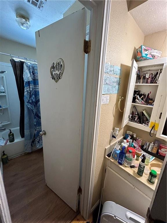 bathroom with shower / bath combo with shower curtain, wood-type flooring, and a textured ceiling