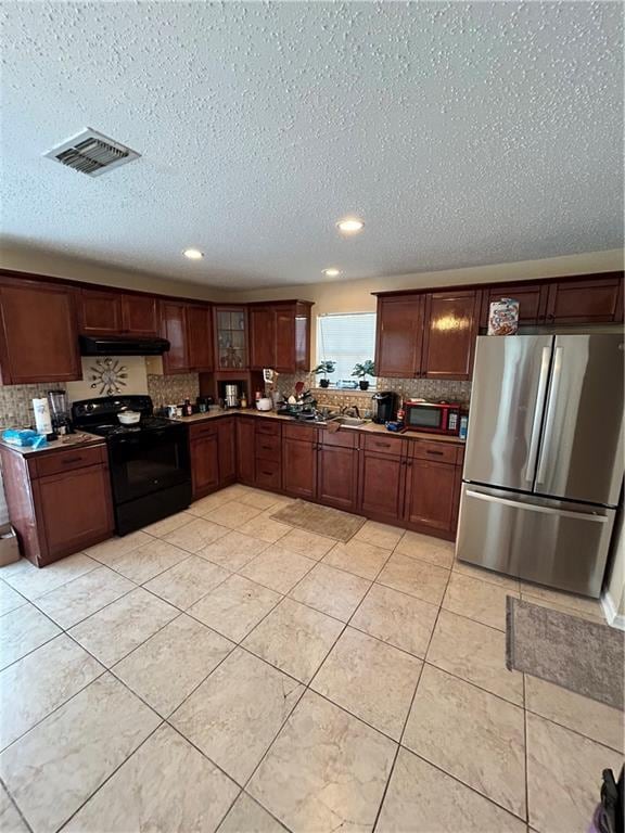 kitchen with a textured ceiling, light tile patterned floors, black electric range, exhaust hood, and stainless steel refrigerator