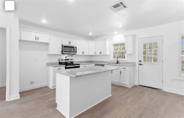 kitchen with appliances with stainless steel finishes, white cabinets, light wood-type flooring, a kitchen island, and sink