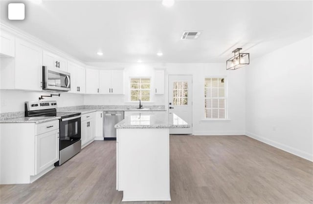 kitchen featuring appliances with stainless steel finishes, white cabinets, light wood-type flooring, and light stone counters