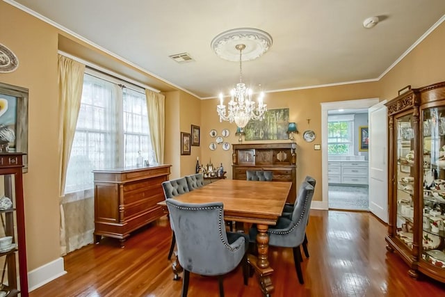 dining space with dark hardwood / wood-style floors, crown molding, and an inviting chandelier