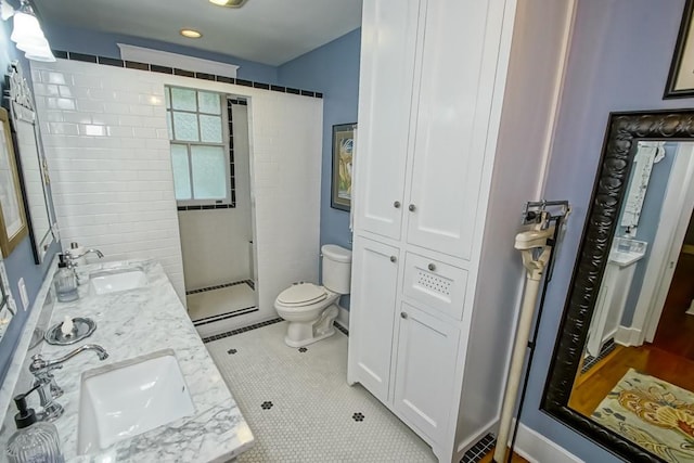 bathroom featuring tiled shower, toilet, dual bowl vanity, and tile patterned flooring